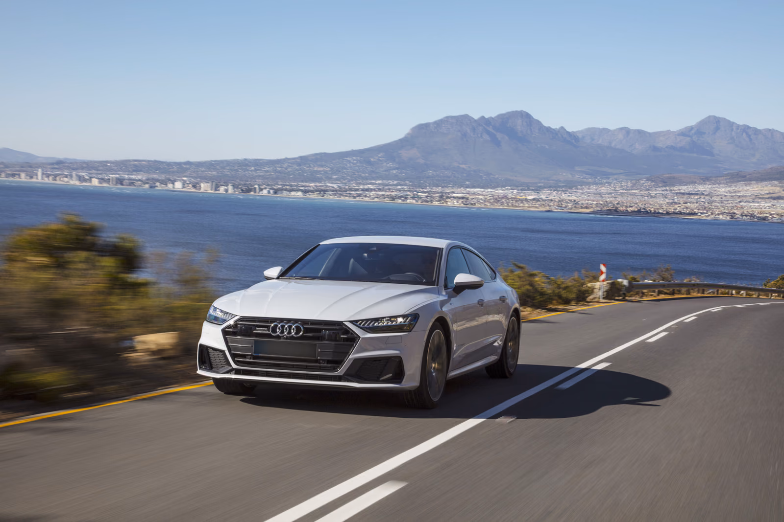 Audi A7 Sportback — серебристый кузов в движении по прибрежной дороге