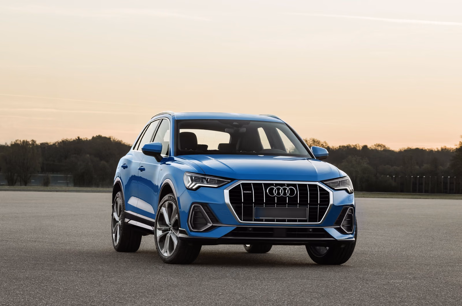Audi Q3 — синий кроссовер спереди в три четверти на закате