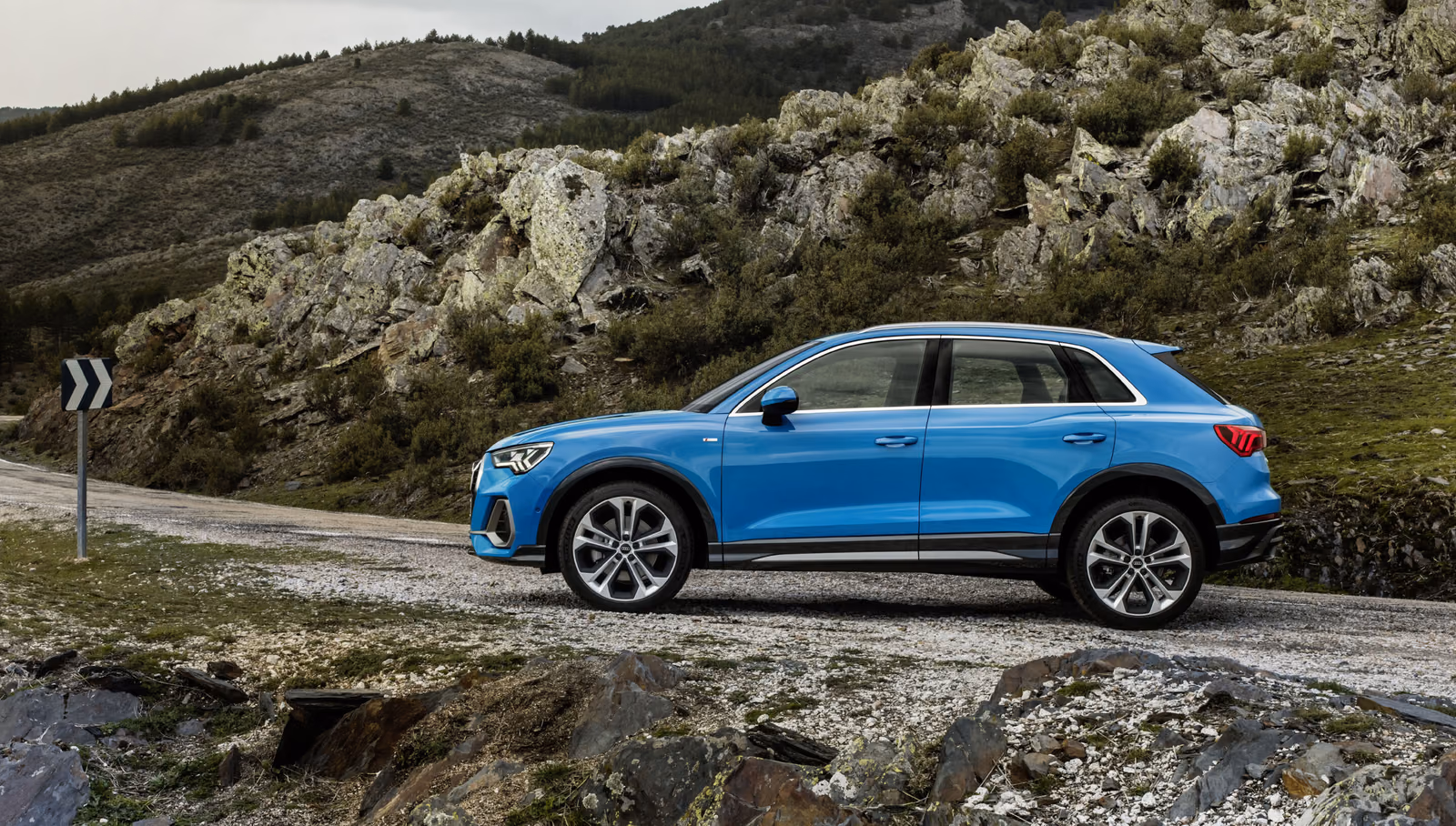 Audi Q3 — профиль синего кузова на горной дороге