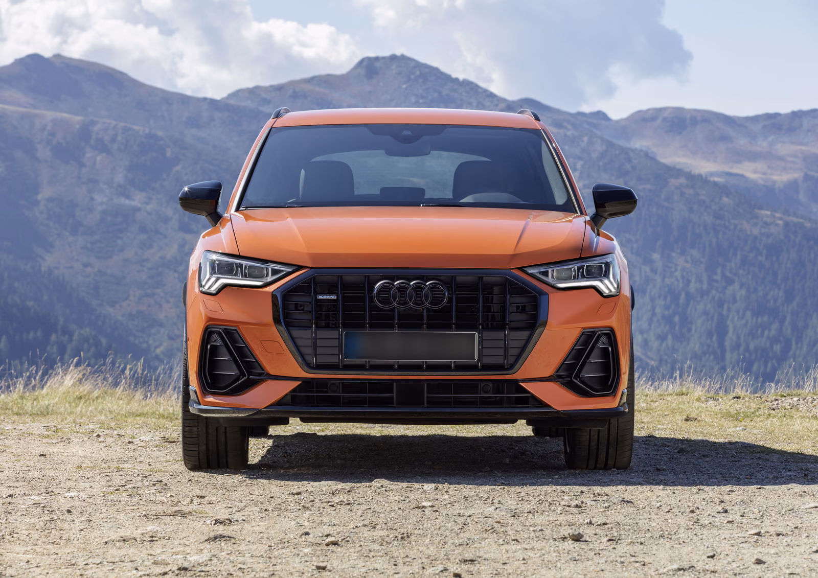 Audi Q3 — оранжевый кузов, вид строго спереди на фоне гор