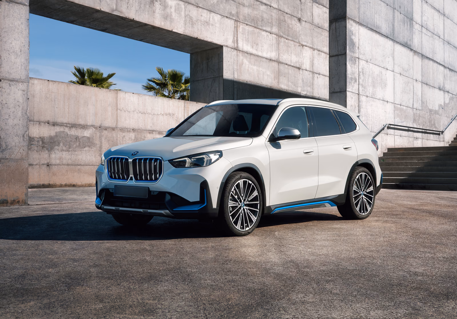 BMW iX1 у бетонного фасада, вид спереди в три четверти