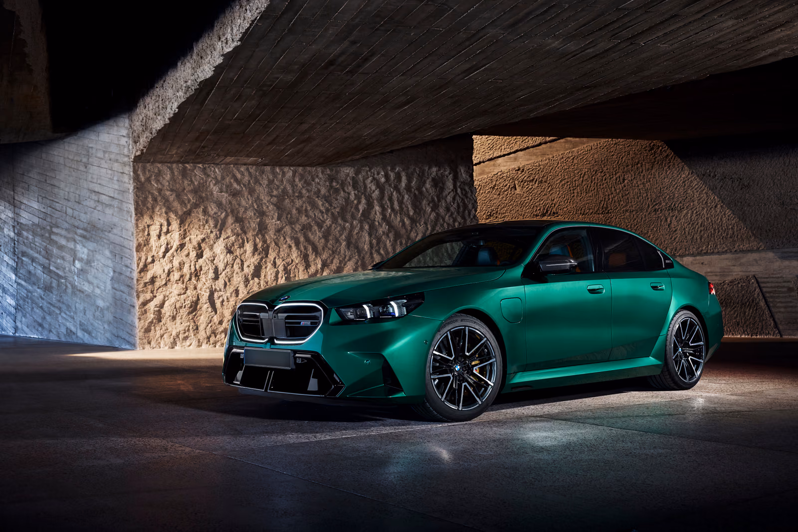 BMW M5 под бетонным навесом, вид спереди в три четверти с подсвеченной оптикой