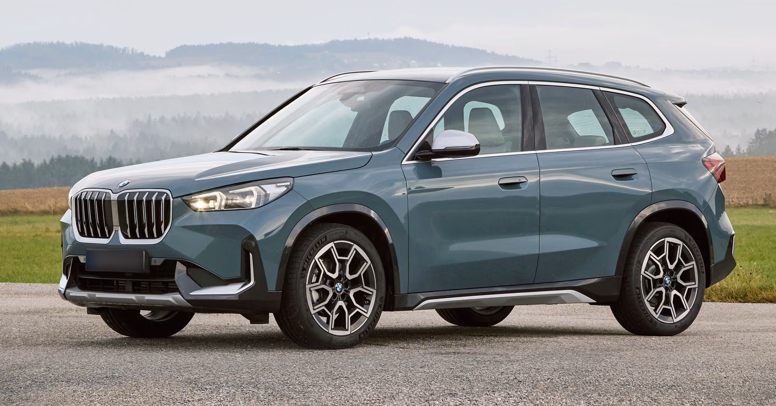 BMW X1 — спереди в три четверти на фоне туманных холмов