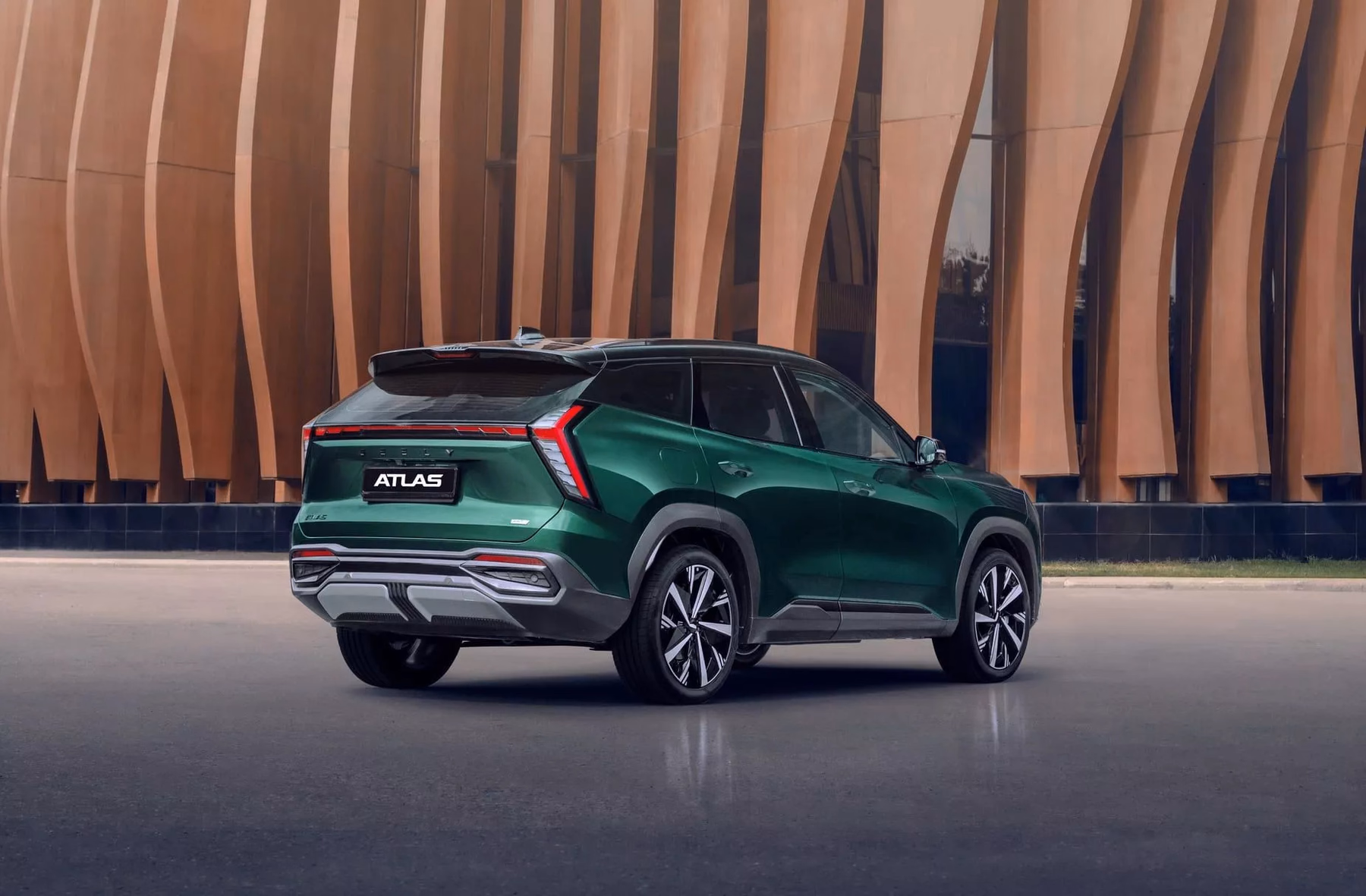 Geely Atlas зелёного цвета у современной архитектуры, вид сзади