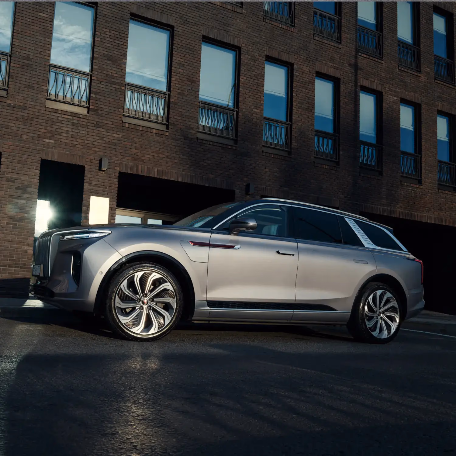 Серебристый Hongqi E-HS9 у кирпичного здания