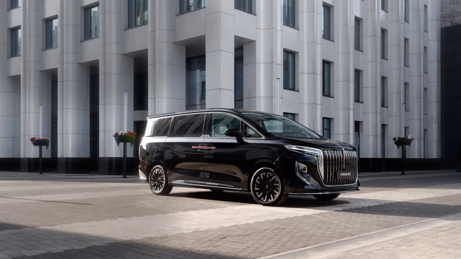 Чёрный HONGQI HQ9 у современного здания, вид спереди в три четверти