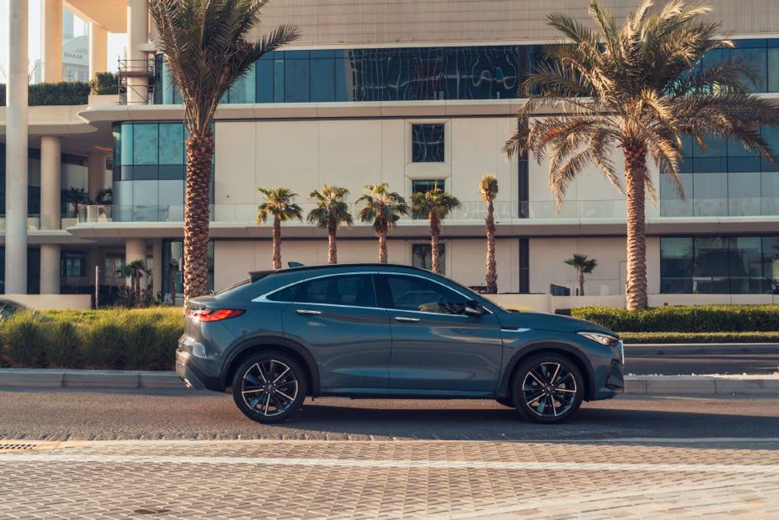 Серый Infiniti QX55 в профиль у современной архитектуры