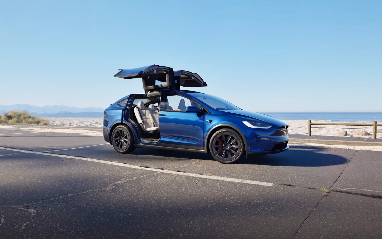 Синяя Tesla Model X с открытыми дверями Falcon Wing у побережья