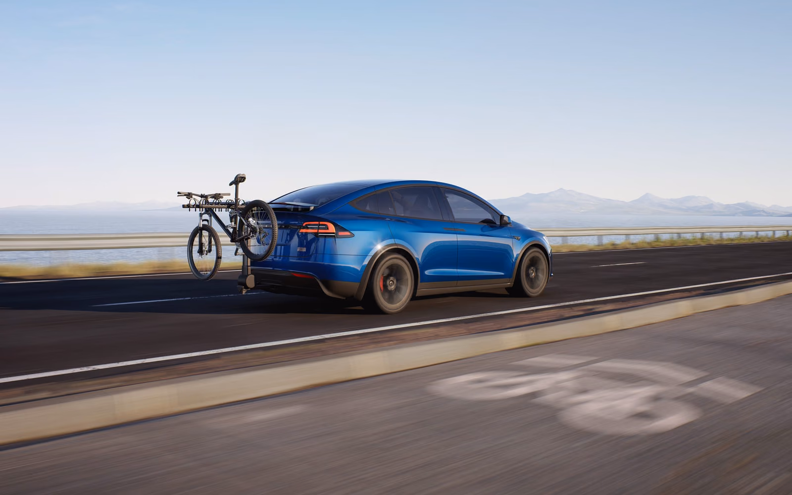 Синяя Tesla Model X с велокреплением на прибрежной дороге