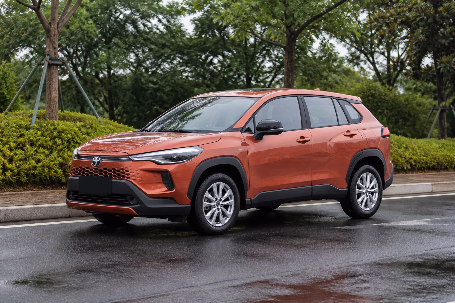 Медная Toyota Corolla Cross на чистой улице у зелёного сквера