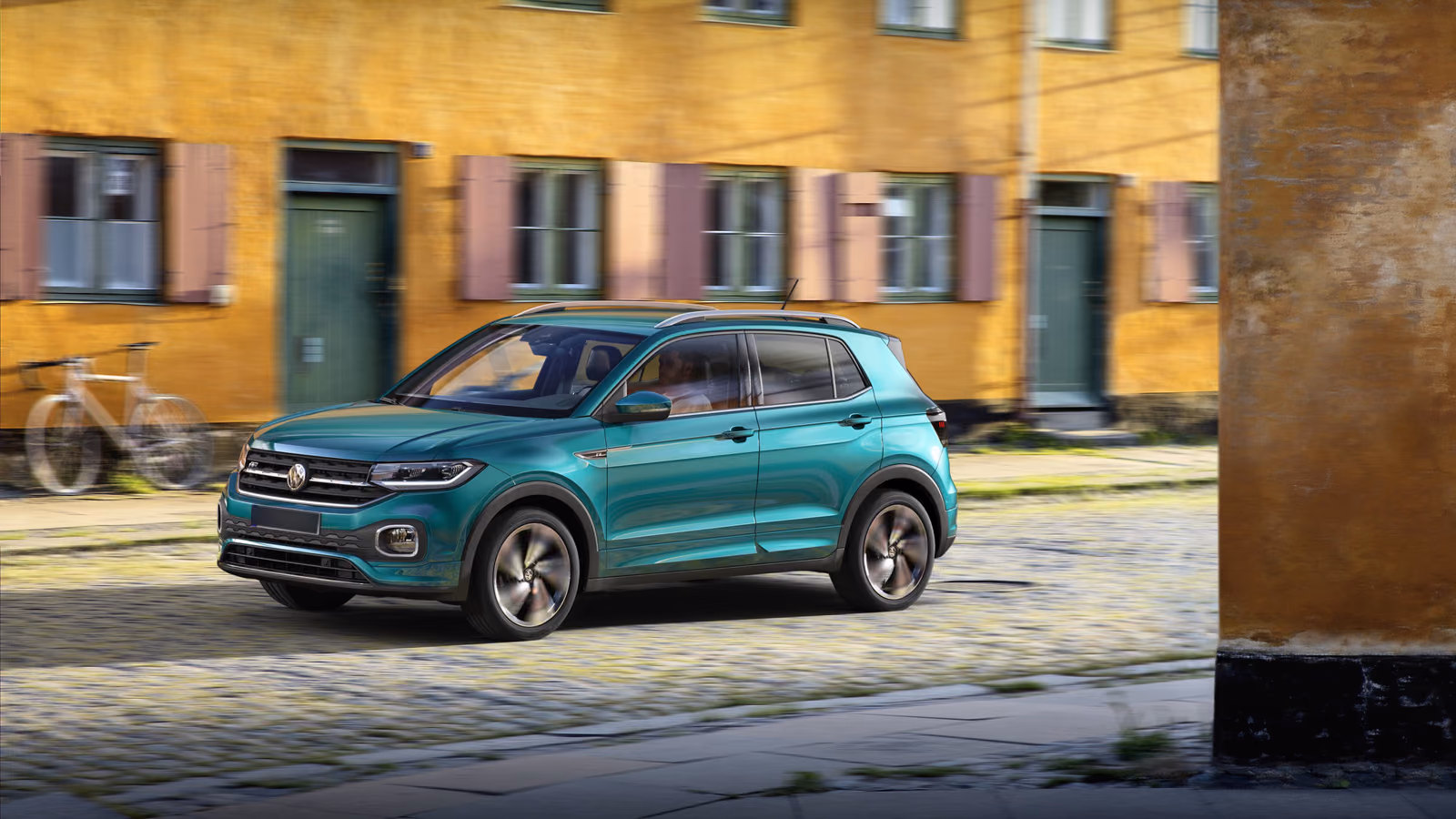 Volkswagen T-Cross у жёлтого дома, вид спереди в три четверти